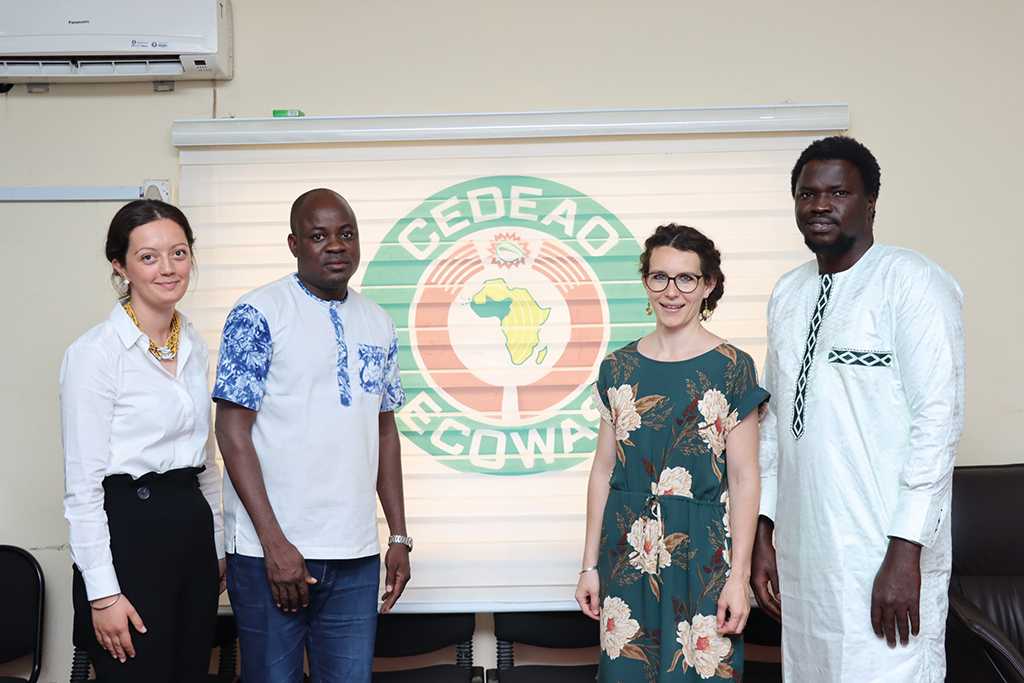 Four people stand in front of a screen on which the ECOWAS logo can be seen: a yellow map of Africa with the West African states colored green, surrounded by a red and a green ring, with the words CEDEAO - ECOWAS.