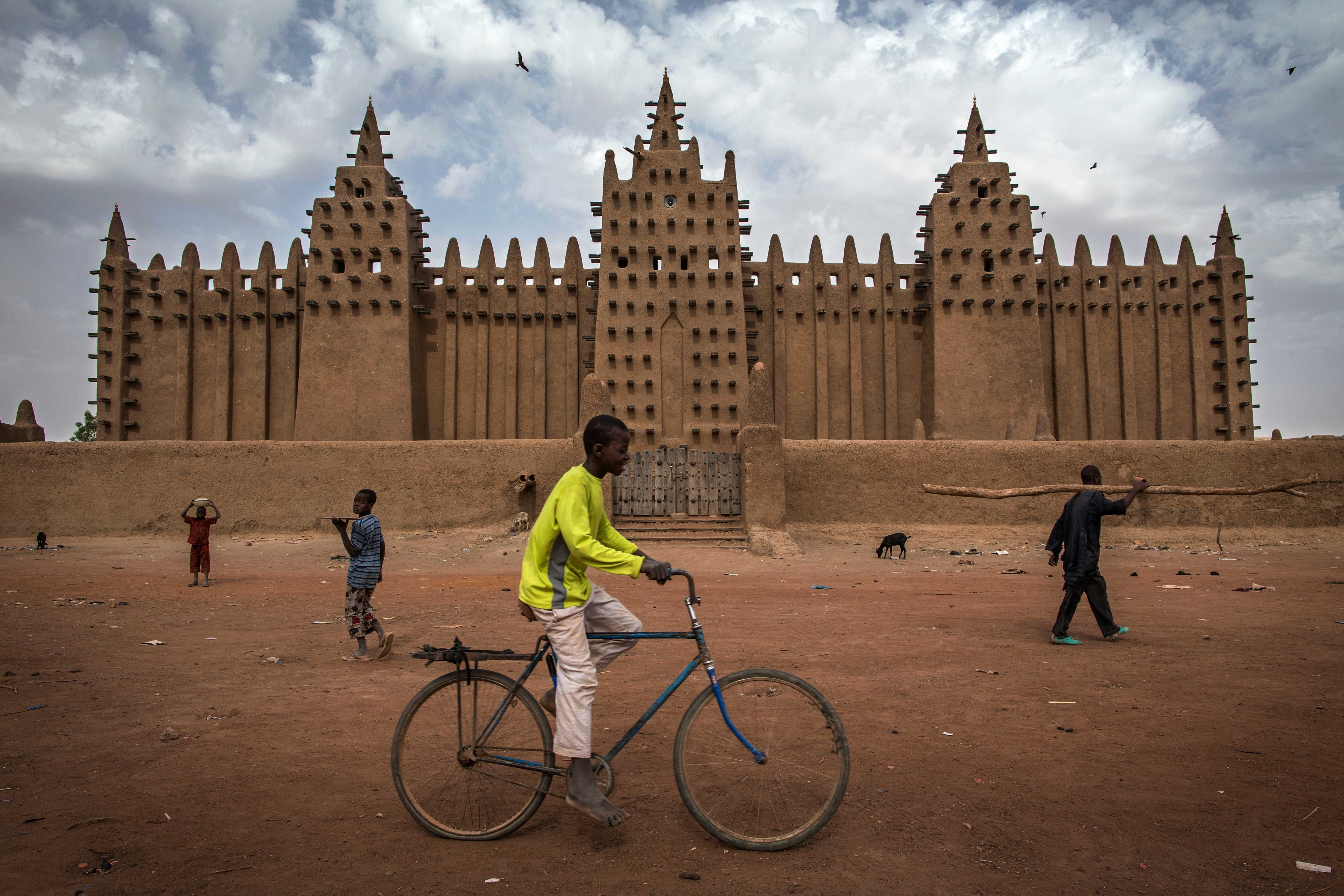 Boy on bicycle in front of a big adobe building