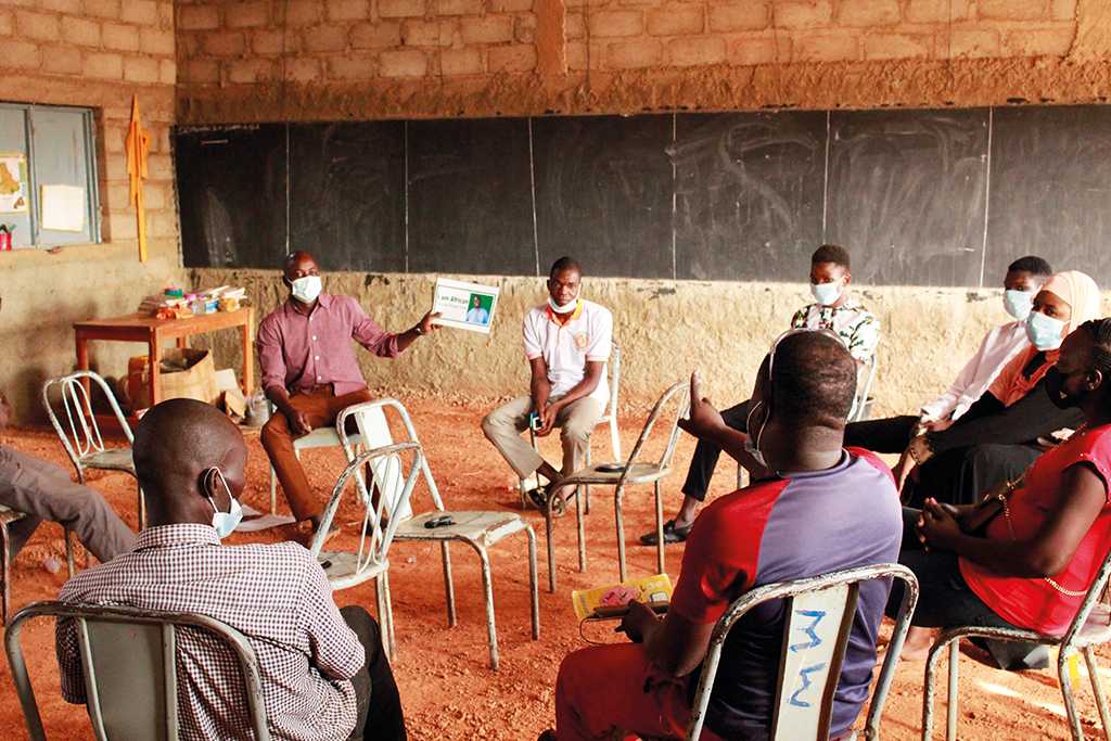 Group of people sitting on metal chairs in a circle. One person holds up a piece of paper.