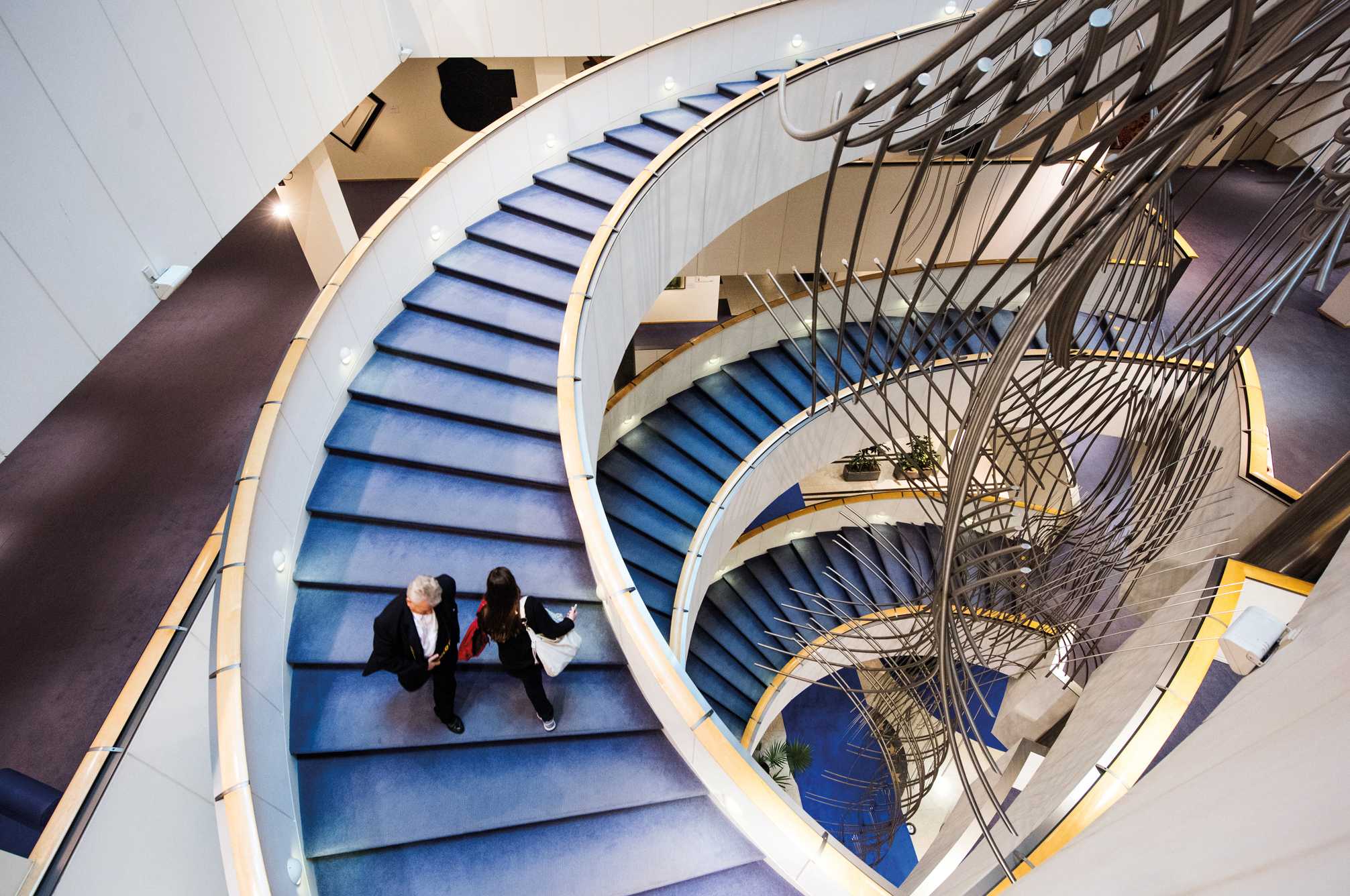 Two people walk up a blue spiral staircase.